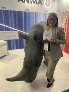 Woman holding a book next to a near life size replica of a rhino; background is graphic representing rising temperatures of earth 1890 to present and logo of asset management firm Anima