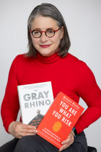 Woman with glasses holding two books, THE GRAY RHINO and YOU ARE WHAT YOU RISK